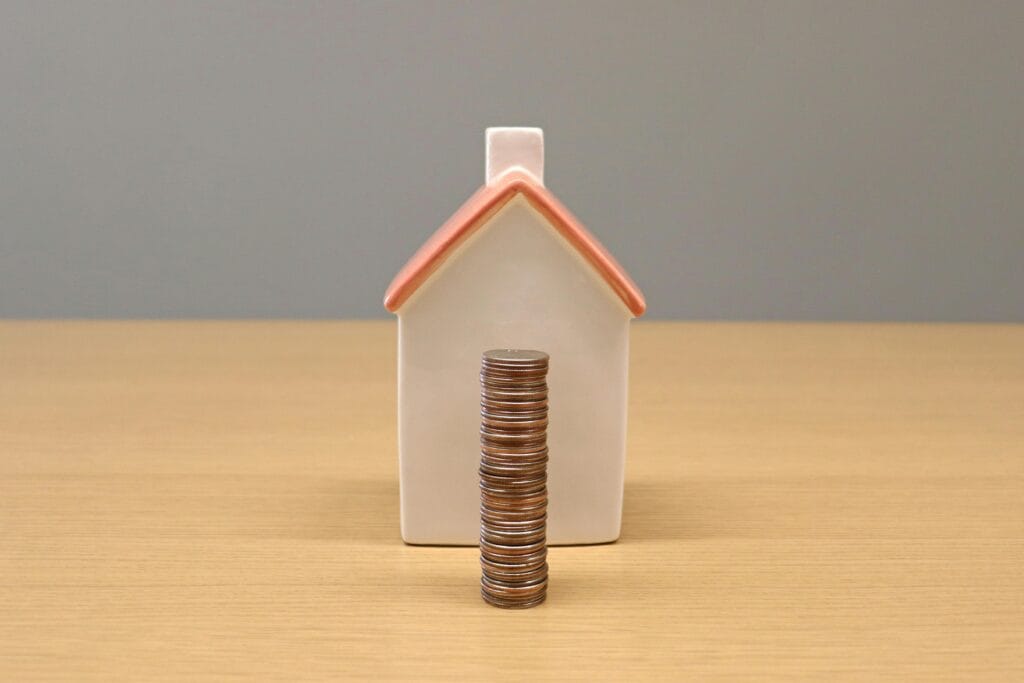 A conceptual still life image of stacked coins in front of a porcelain house, symbolizing savings and investment.